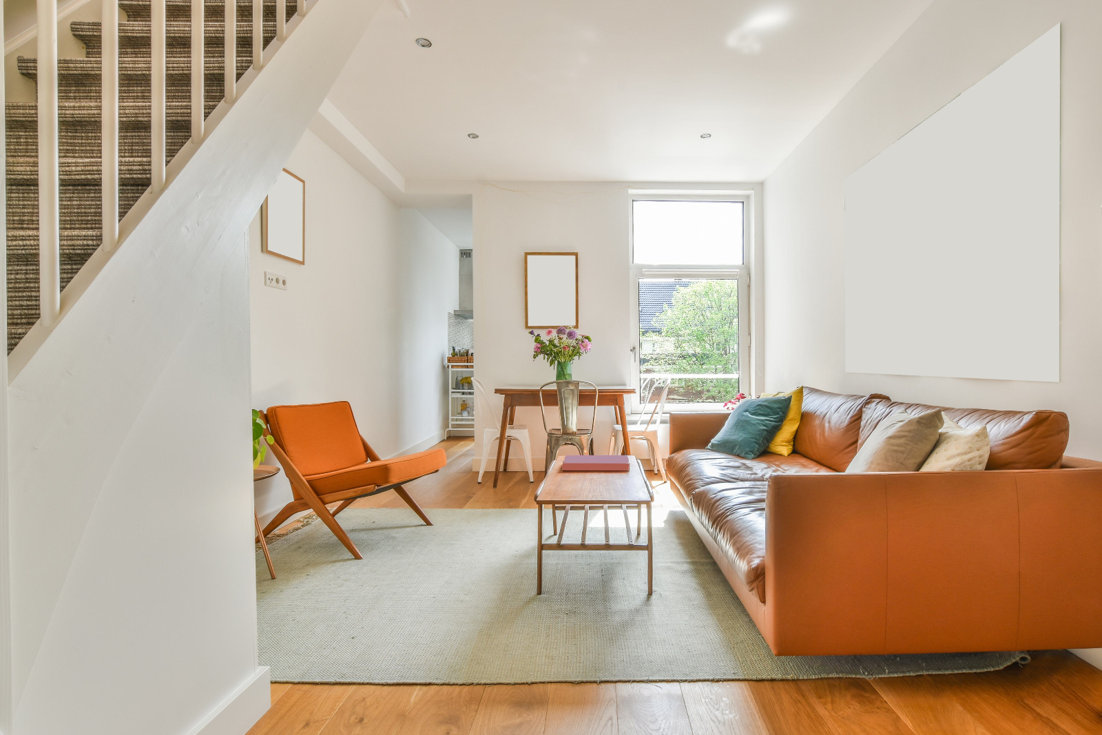 Bright living and dining room with a tan leather sofa, orange armchair and stairs